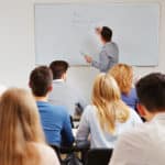 Instructor writing on whiteboard in front of students. What is Lecture Capture?